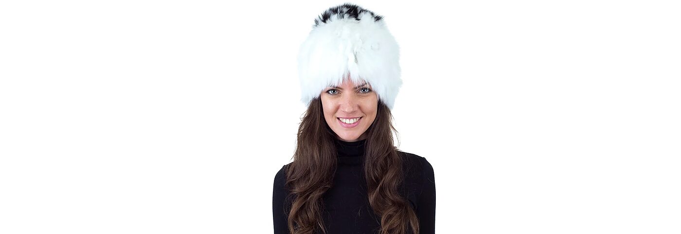A smiling woman in a white fur hat with a black-and-white crown, black turtleneck